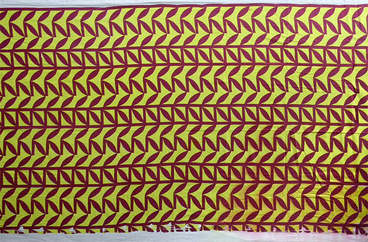 Vibrant yellow fabric with a simple leaf repeating pattern that is maroon.