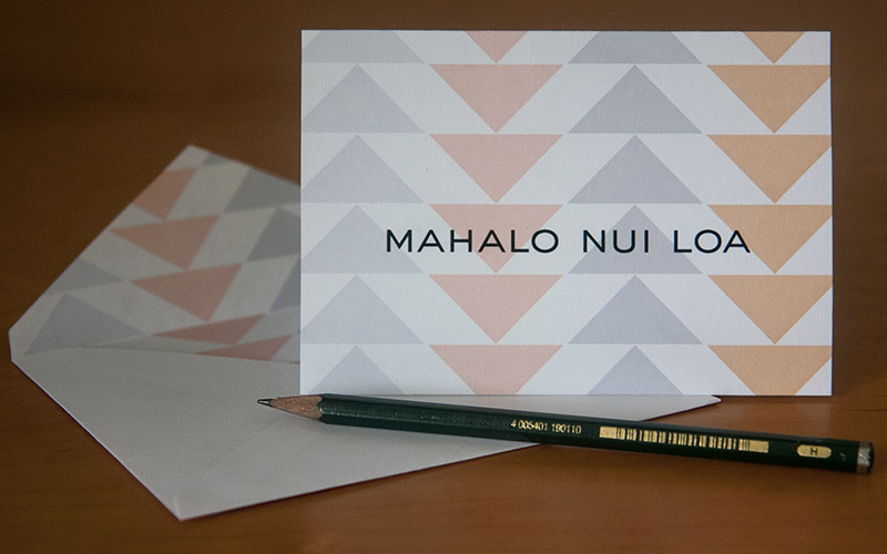 Pastel Hawaiian triangle greeting card which reads: Mahalo nui loa, resting upright on envelope.