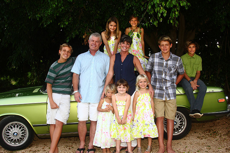Two adults with eight children in front of vintage car.
