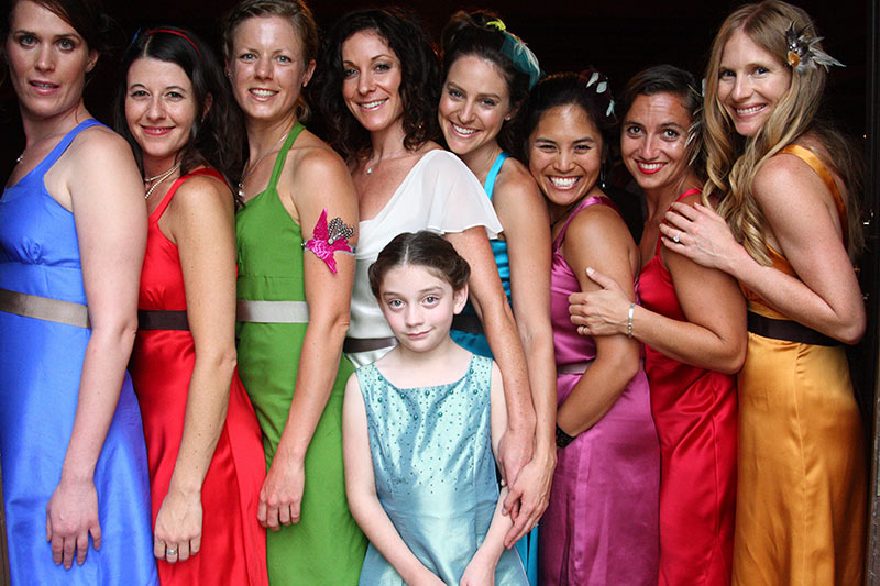 Eight women in colorful dresses with child in front.